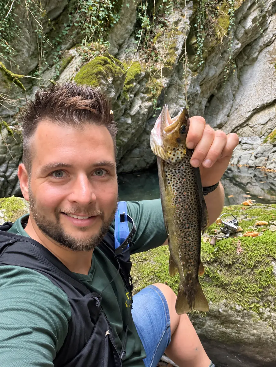 Pêcheur présentant une truite fario près d’une rivière bordée de rochers