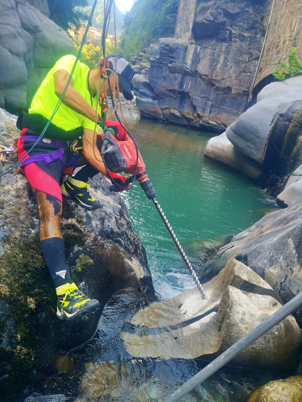 Intervenant utilisant un perforateur sur un bloc rocheux au bord d’une rivière.