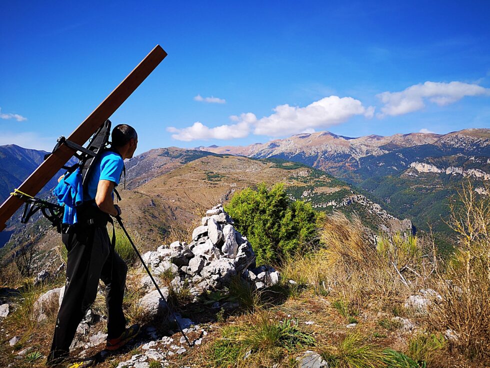 Transport à dos d’homme d’un poteau en bois sur un sentier de montagne.