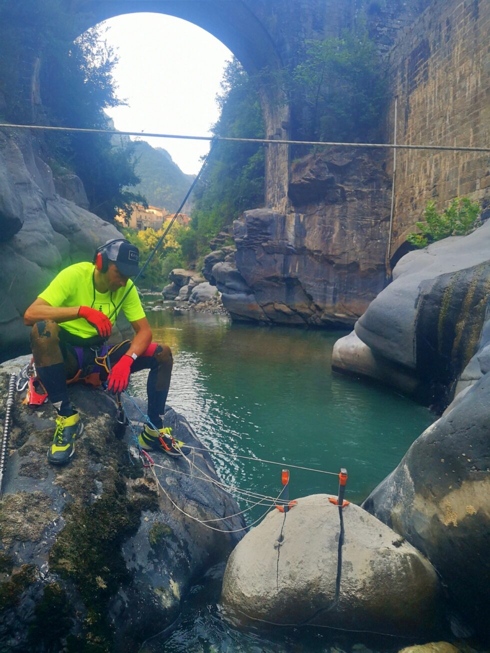 Intervenant équipé pour des travaux sur rocher en bord de rivière, sous un pont en pierre.