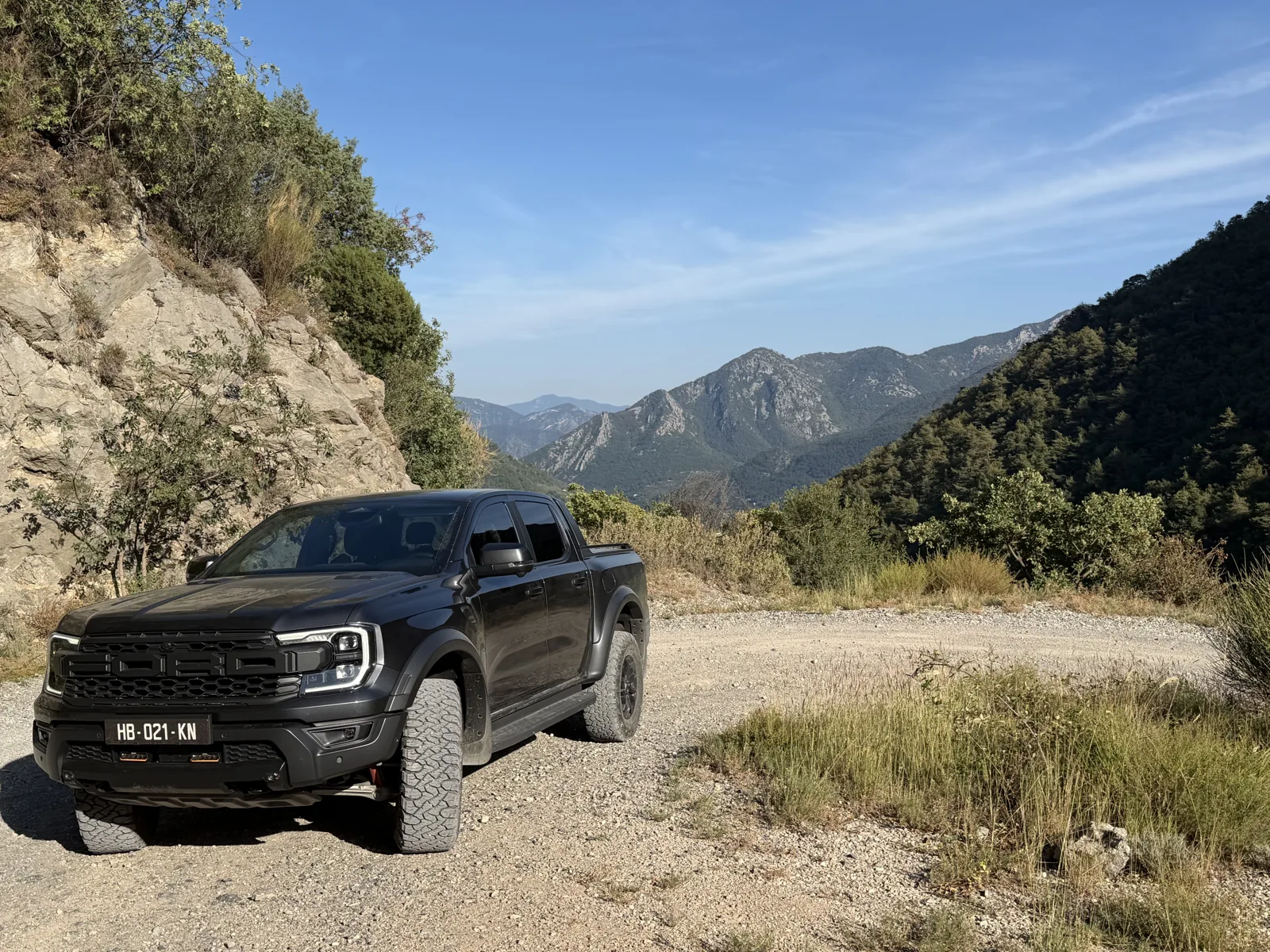 4x4 noir sur une piste, au pied d’une paroi rocheuse sous un ciel bleu.