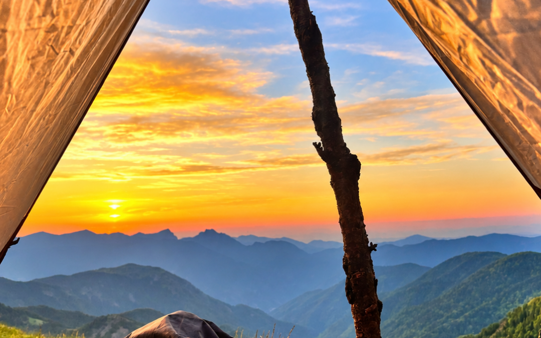 Vue depuis un abri de bivouac ouvert sur les montagnes et un ciel doré au soleil rasant.