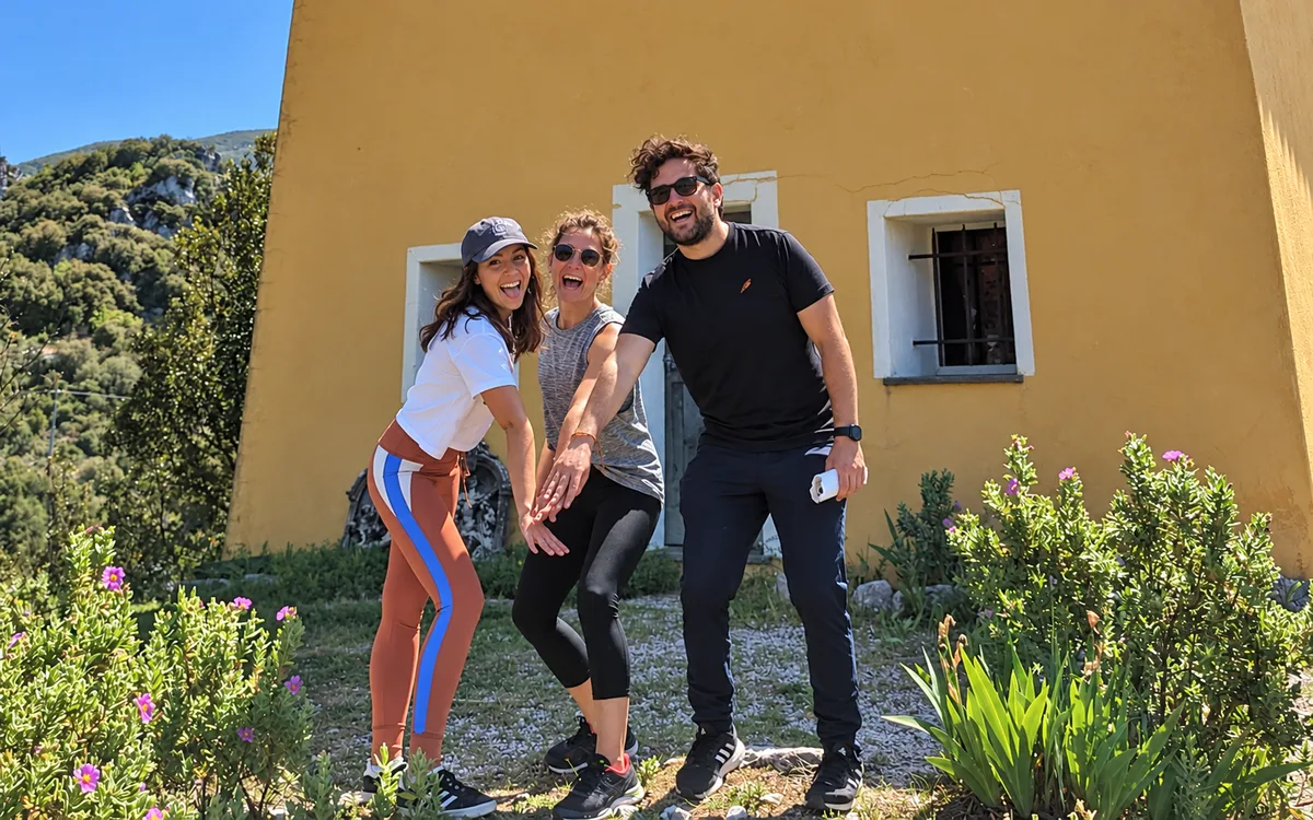 Trois participants sourient et réunissent leurs mains devant une façade jaune.