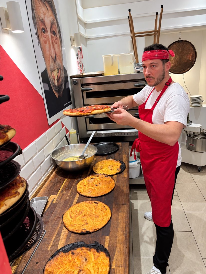 Un cuisinier en tablier rouge tient une préparation devant le four.