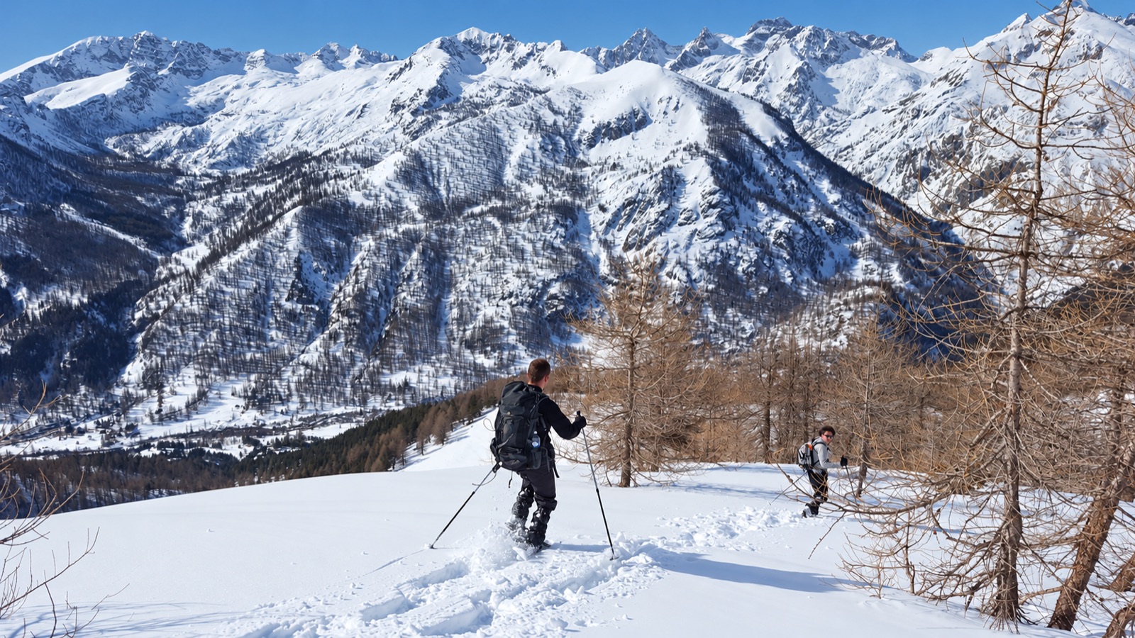 Deux randonneurs en raquettes devant un panorama de sommets enneigés