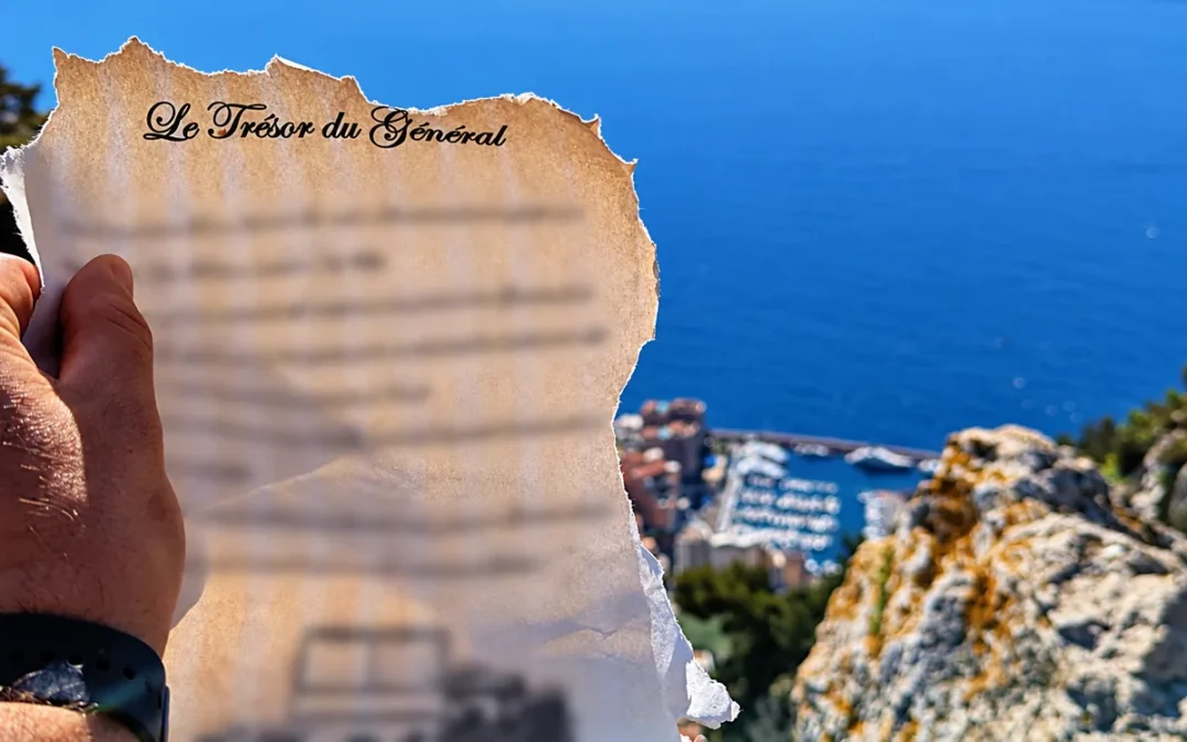 Une main tient le roadbook du Trésor du Général devant la mer ; le texte du jeu est flouté.