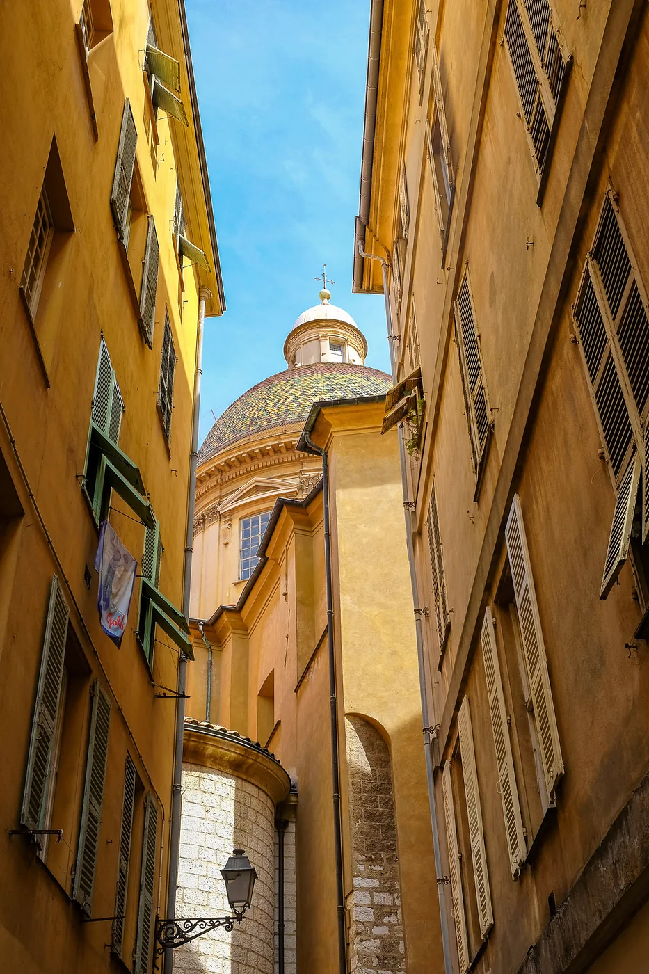 Ruelle aux façades ocres ouvrant sur un dôme dans le Vieux-Nice.